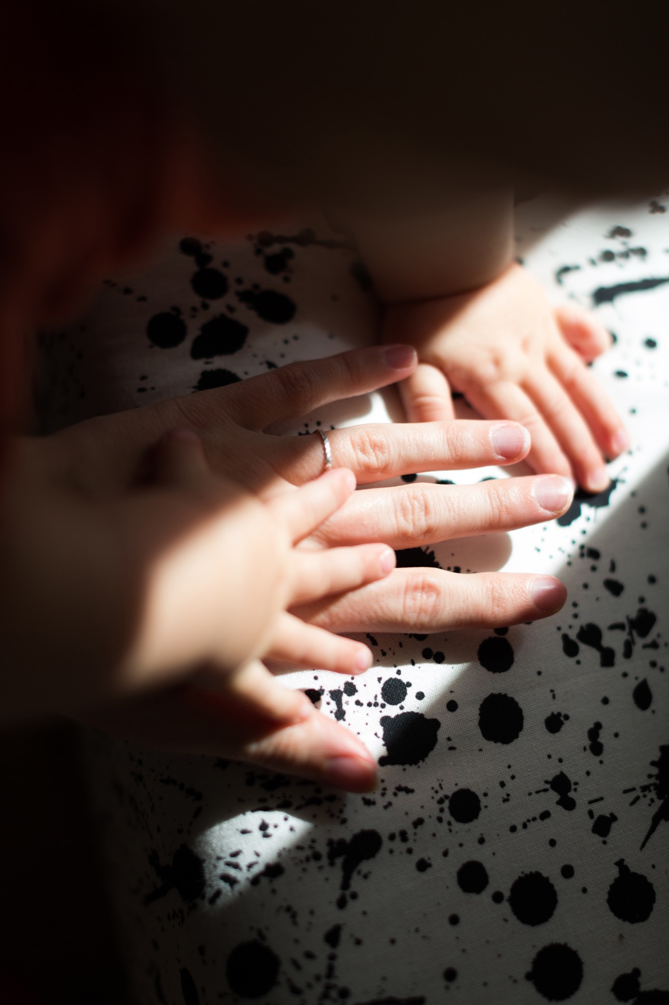 A parent's hand and a baby's hands on a patterned blanket.